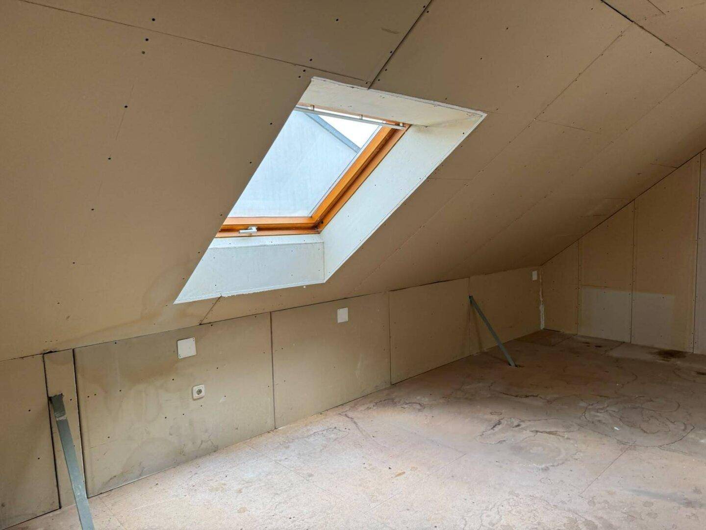Nahaufnahme eines Dachfensters im unausgebauten Dachboden, das Tageslicht hereinlässt.