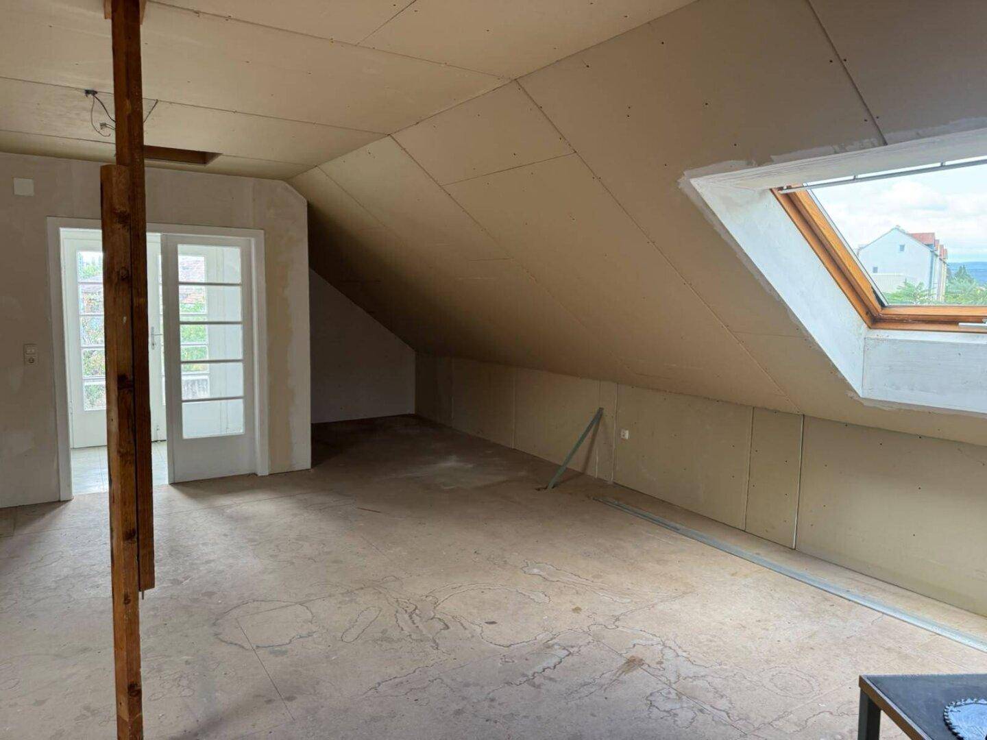 Blick auf den unausgebauten Dachboden mit Tür, Dachfenster und schrägen Decken.