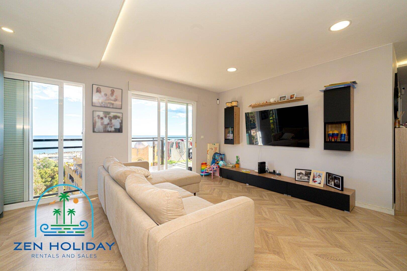 Heller Wohnbereich mit bequemem Sofa, Fernseher und großen Schiebetüren zum Balkon mit Meerblick.