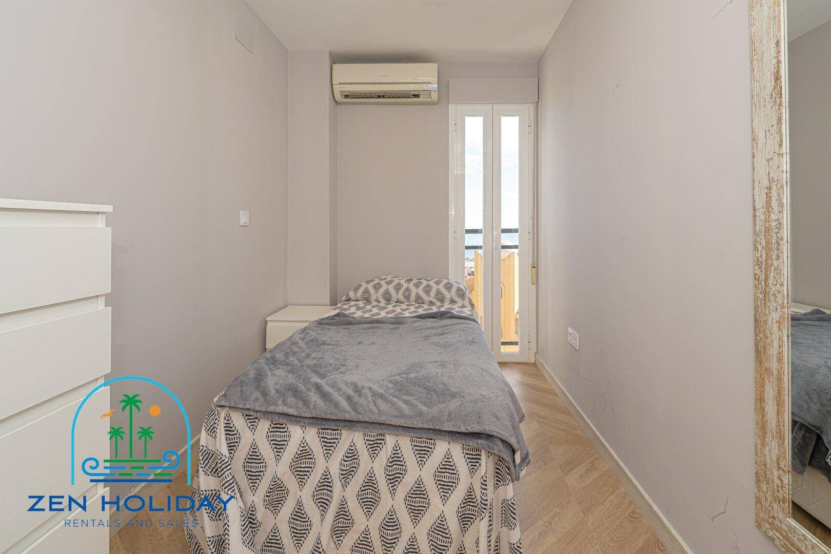 Gemütliches Schlafzimmer mit Einzelbett, weißer Kommode und Zugang zu einem kleinen Balkon.