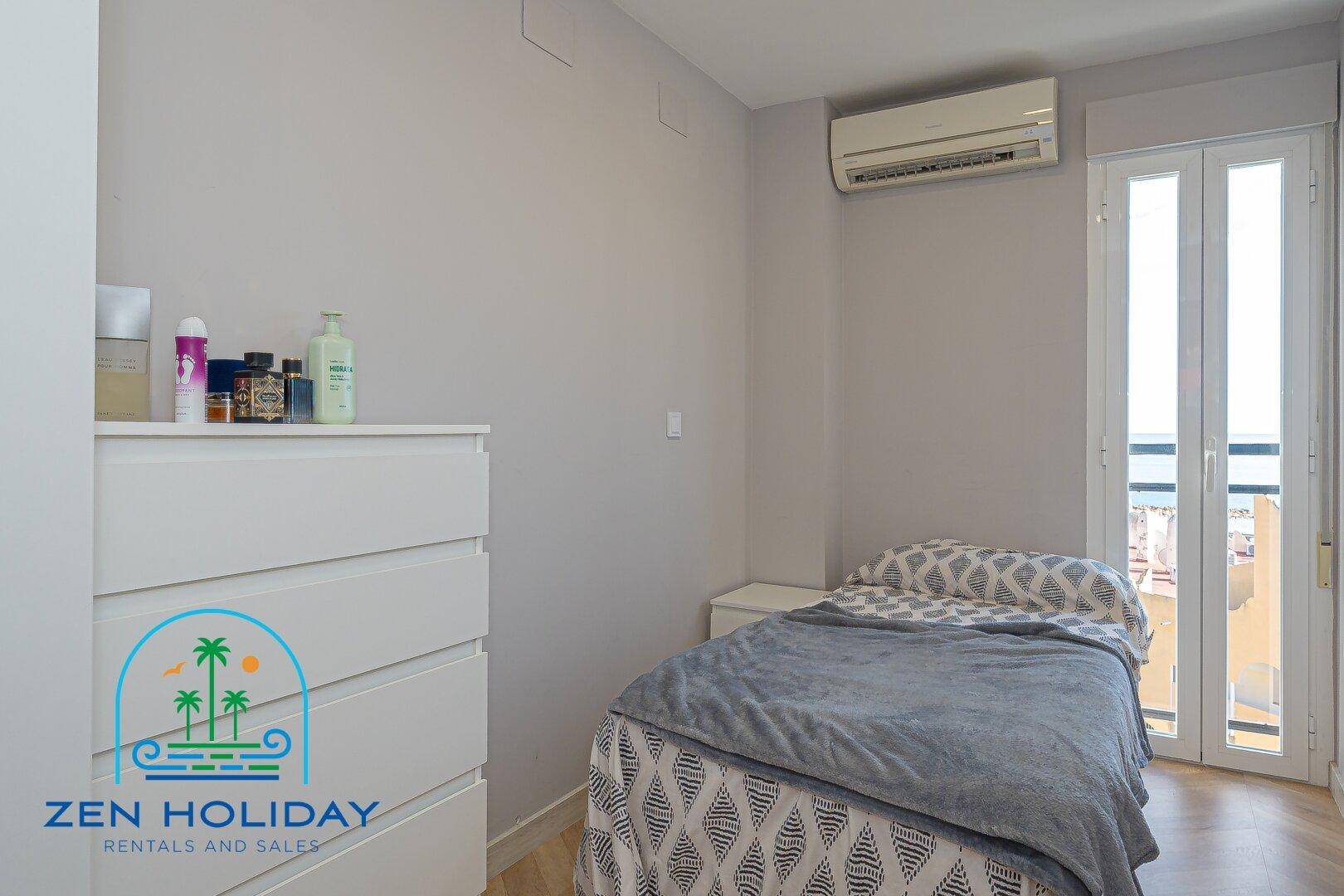 Helles Schlafzimmer mit Einzelbett, weißer Kommode und Balkontür, gut beleuchtet.