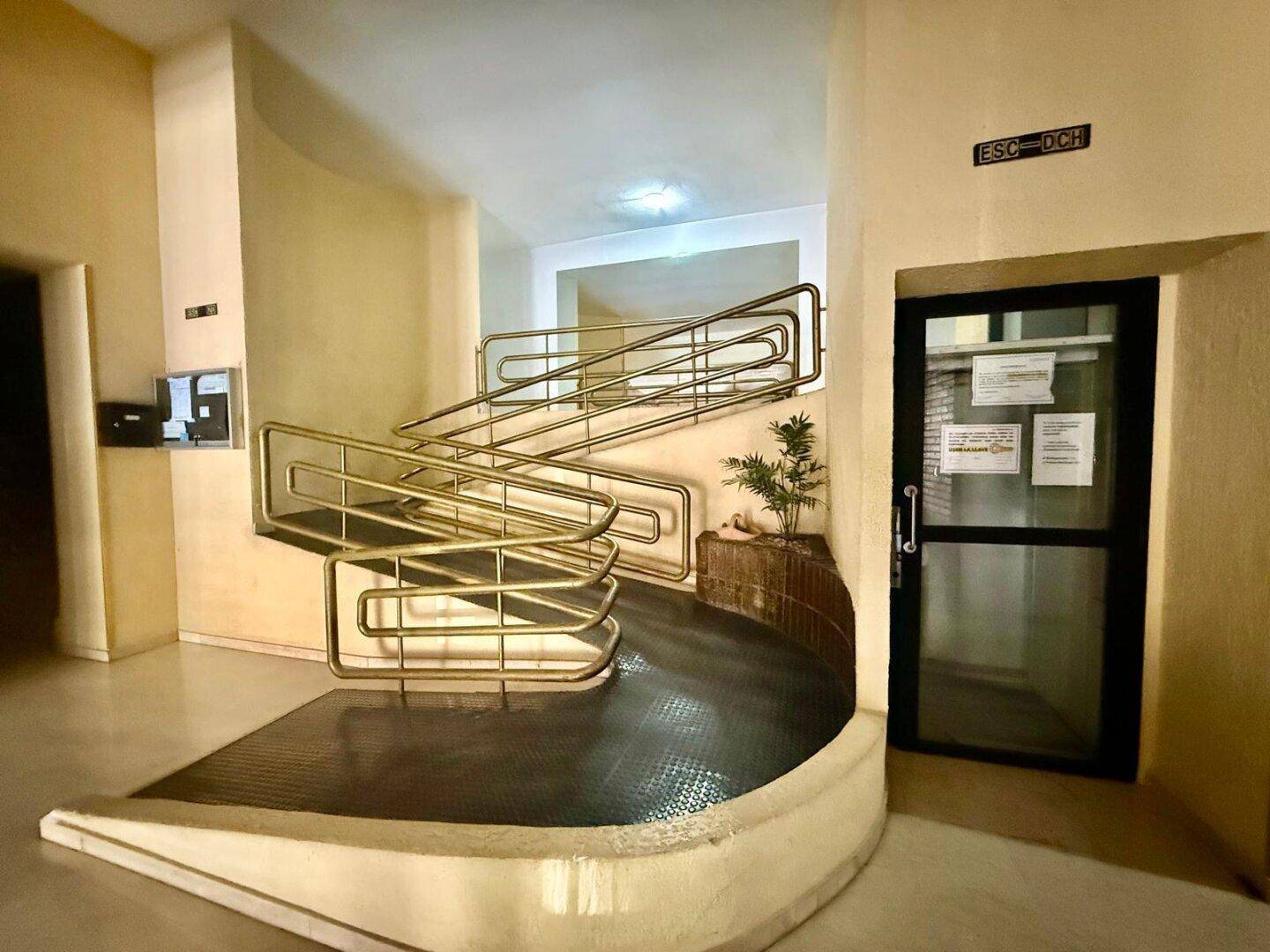 Eingangsbereich mit Rampe und Treppe, ausgestattet mit goldenen Handläufen für Barrierefreiheit.