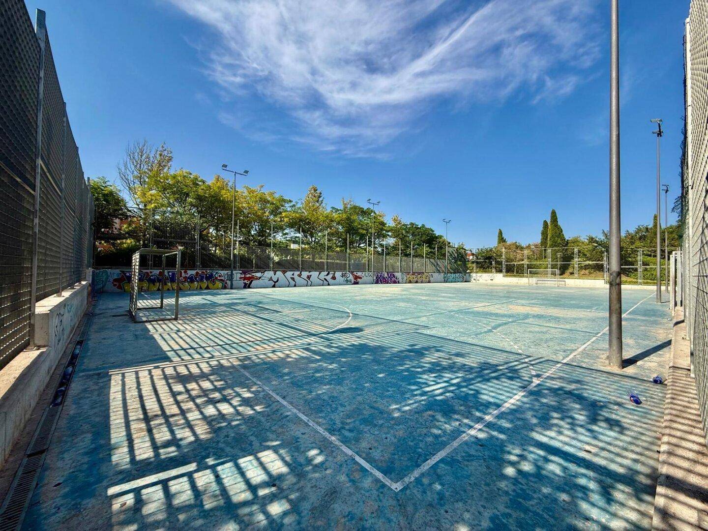Mehrzweck-Sportplatz im Freien mit Zäunen, geeignet für verschiedene Ballspiele.