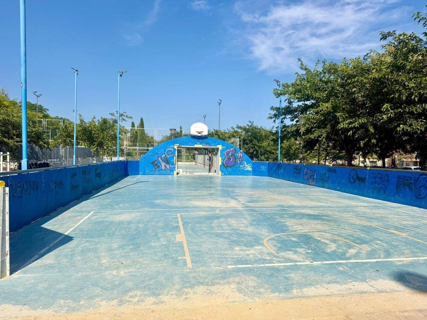 Blauer Basketballplatz im Freien, umgeben von Bäumen, ideal für sportliche Aktivitäten.