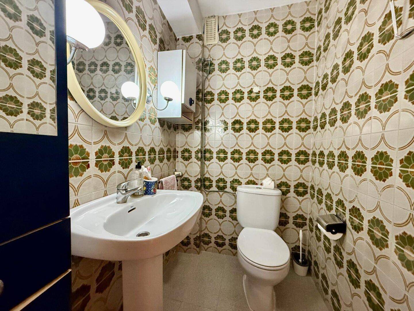 Badezimmer mit auffälligen grünen und weißen Fliesen, Waschbecken und Toilette.