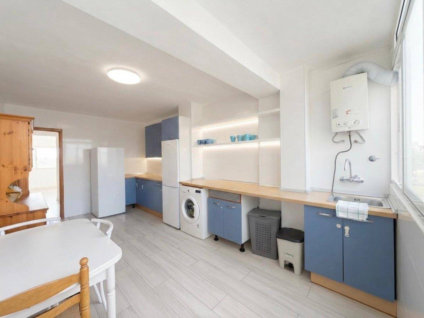 Helle Küche mit blauen Schränken, viel Arbeitsfläche und modernen Geräten, inklusive Kühlschrank.