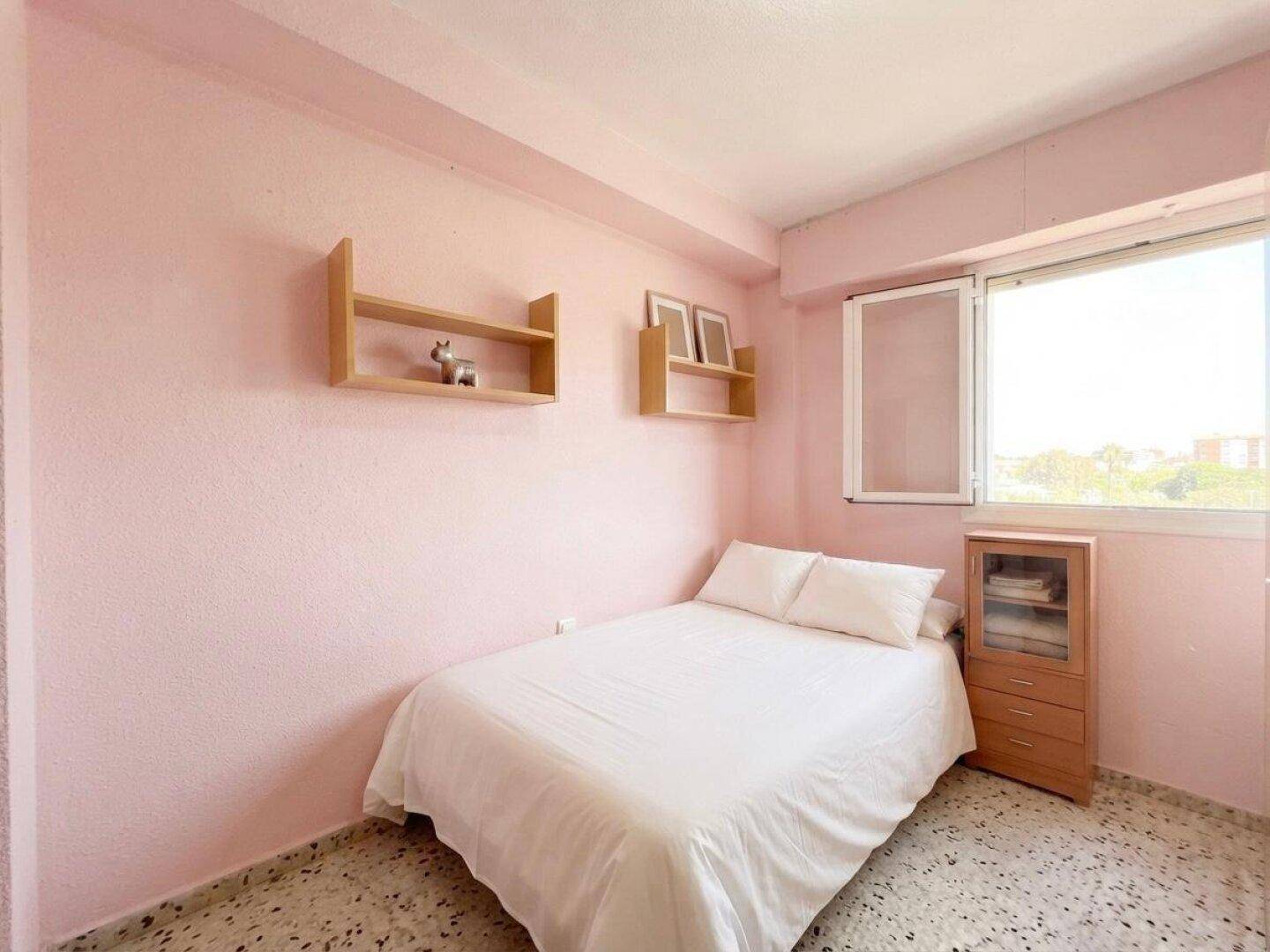 Helles Kinder- oder Gästezimmer mit Einzelbett, rosa Wänden und einem Fenster.