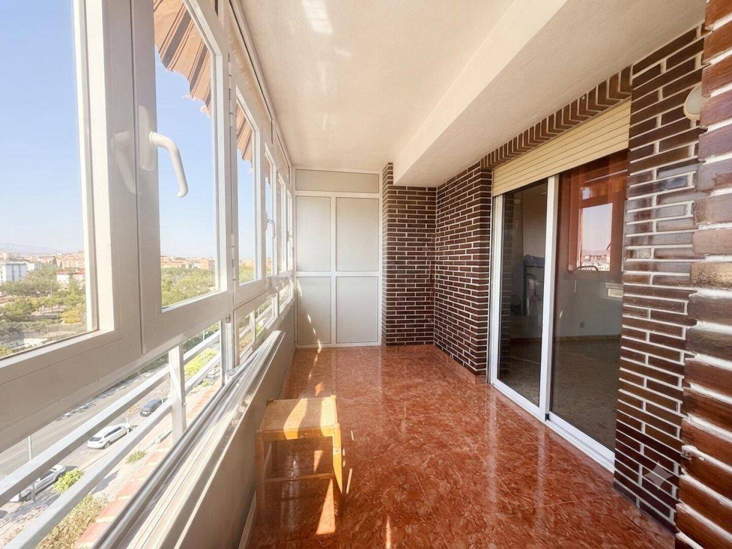 Verglaster Balkon mit Terrakotta-Fliesen und Blick auf die Stadt, ideal für entspannte Stunden.