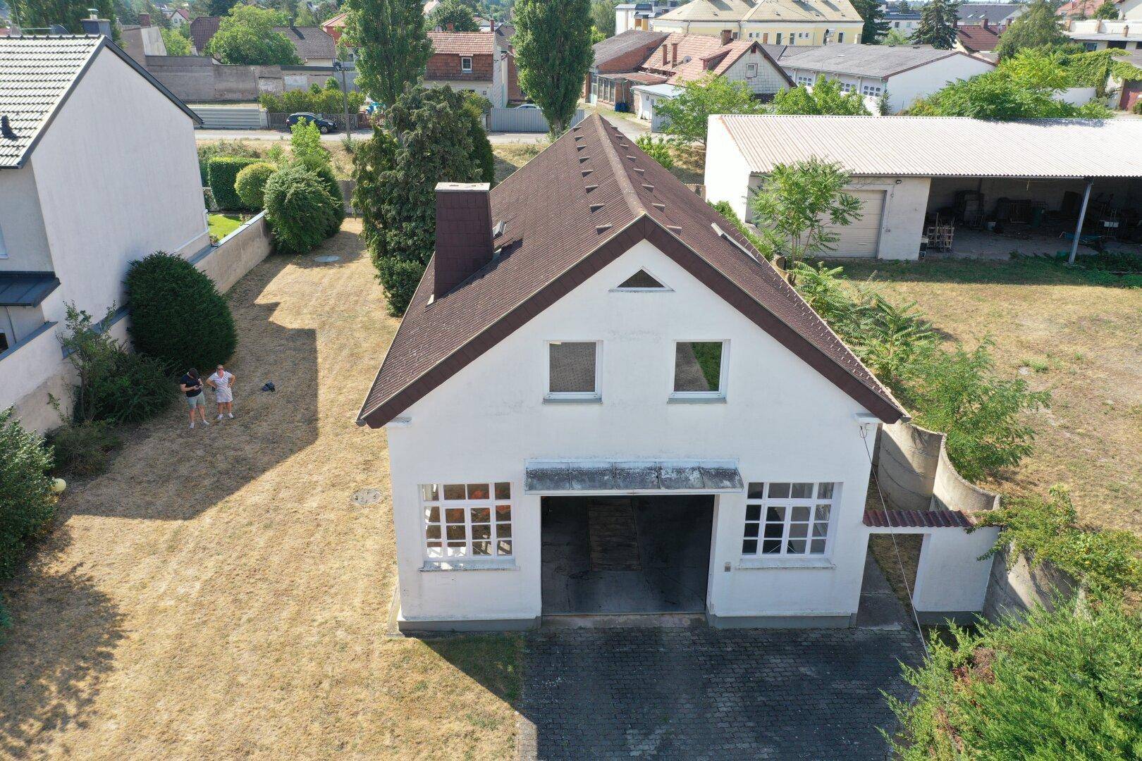 Luftaufnahme eines weißen Hauses mit braunem Dach, großem Garagentor und trockenem Rasen.