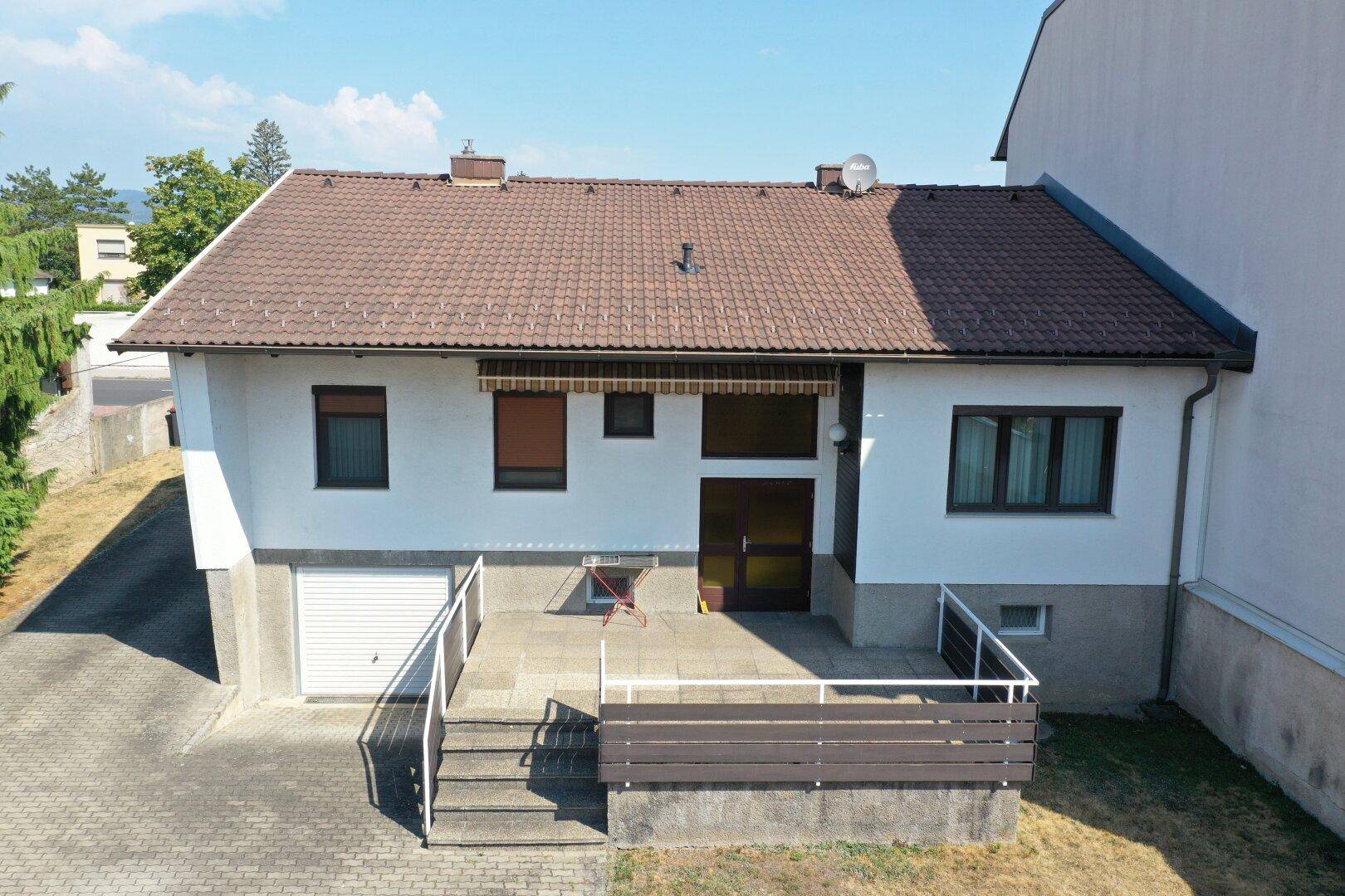 Luftaufnahme der Hausfront mit braunem Ziegeldach, weißer Fassade und gepflastertem Eingangsbereich.