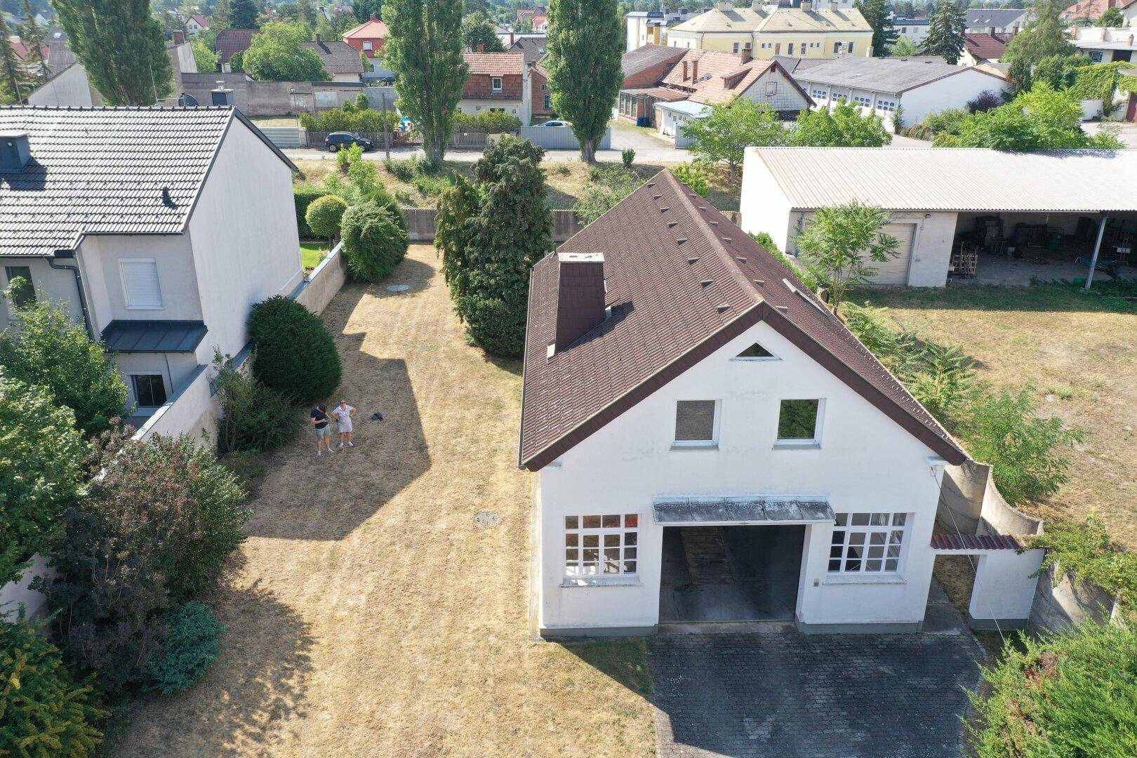 Luftaufnahme eines weißen Hauses mit braunem Dach, großem Garagentor und trockenem Rasen.