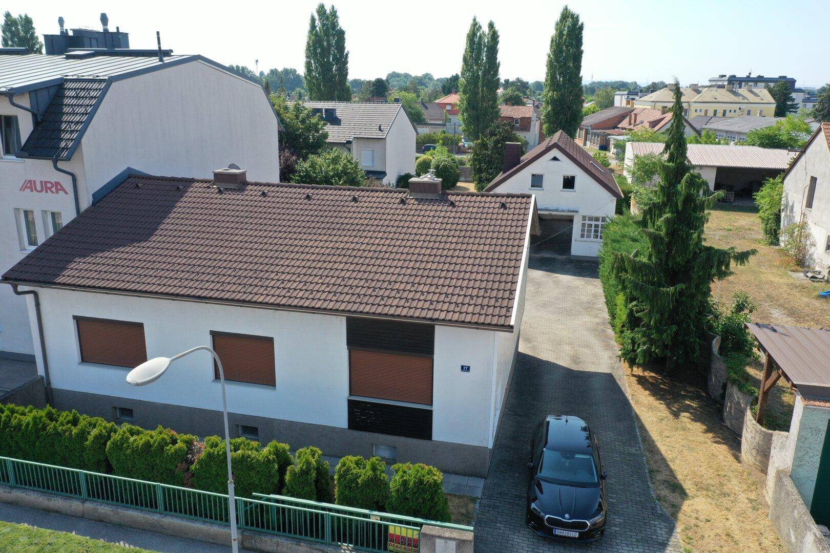 Luftaufnahme eines Hauses von der Straße aus mit geparktem Auto und grüner Hecke.