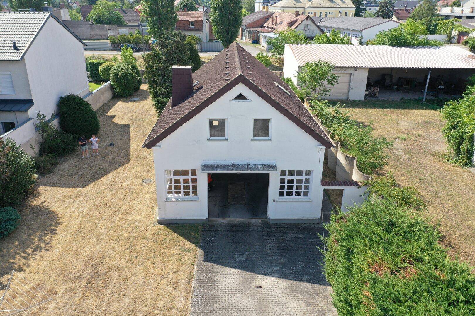 Luftaufnahme eines weißen Hauses mit braunem Dach, großem Garagentor und trockenem Rasen.