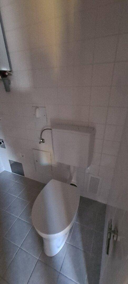 Nahaufnahme einer Toilette in einem Badezimmer mit weißen Fliesen an Wänden und Boden.