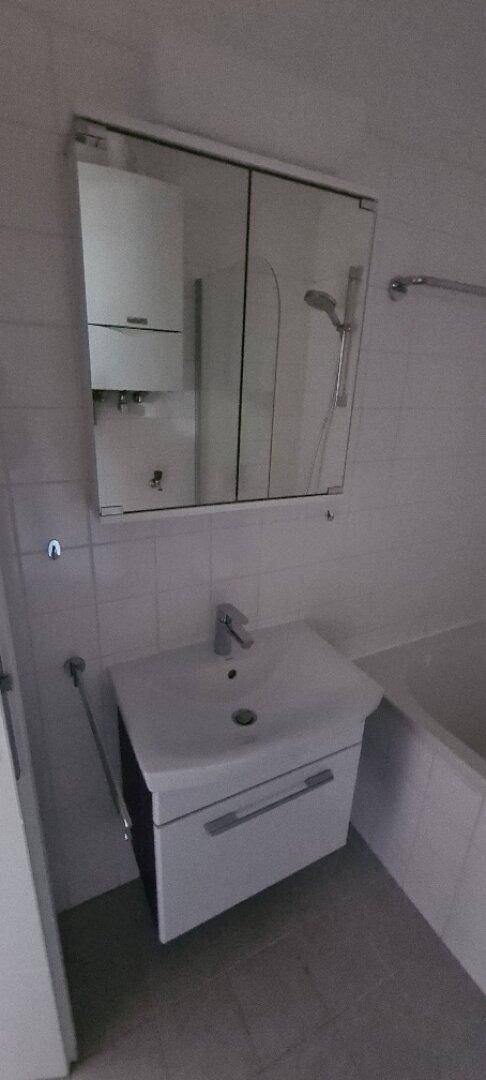 Badezimmer mit Waschbecken, Spiegelschrank und Badewanne, ausgestattet mit hellen Fliesen.