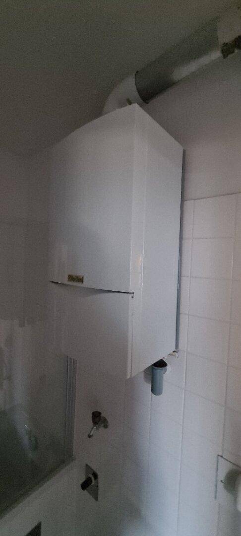 Wandmontierter Warmwasserbereiter in einem gefliesten Badezimmer, bereit zur Nutzung.