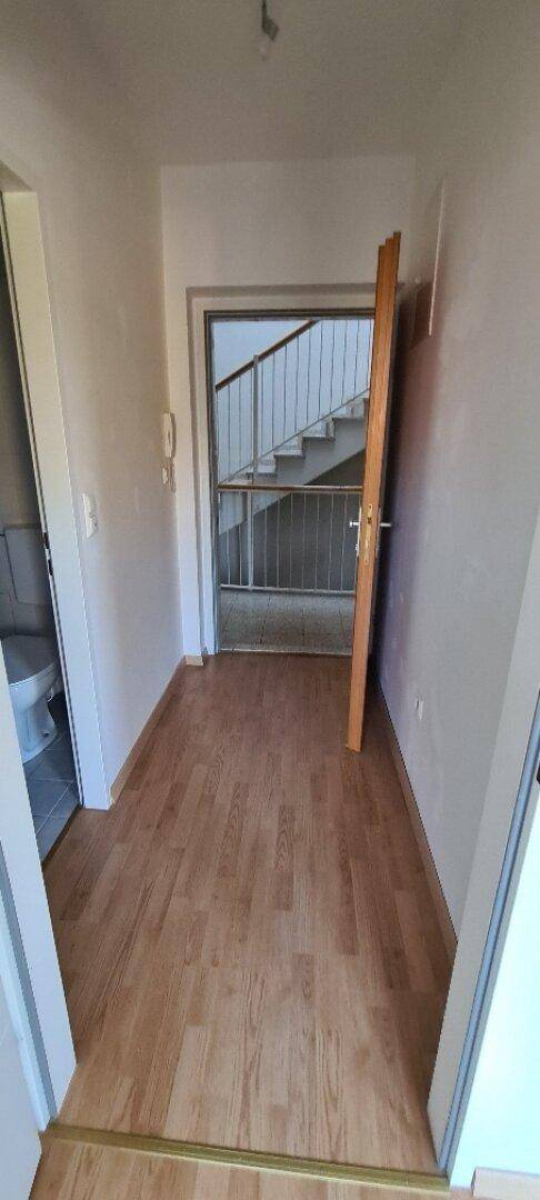 Flur mit Holzboden und Zugang zu einem WC sowie einem Treppenhaus im Hintergrund.
