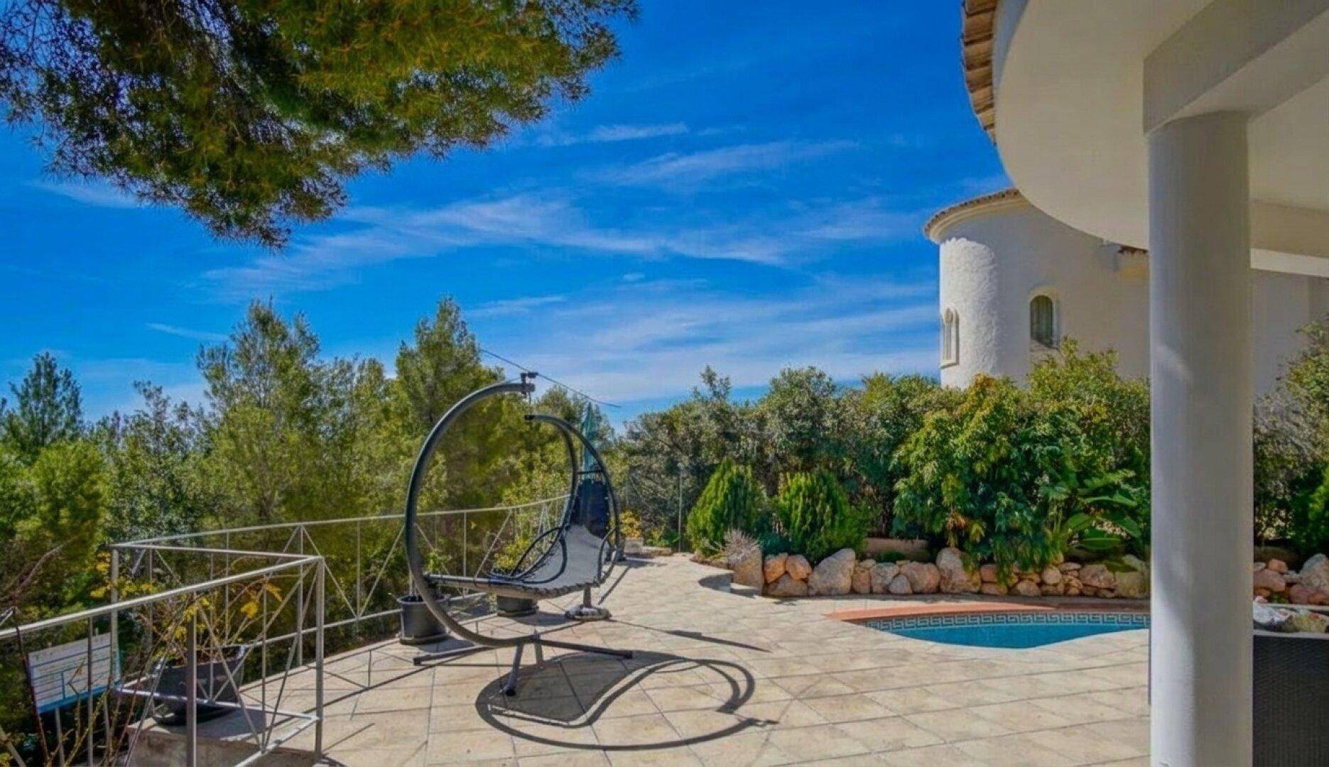 Geräumige Terrasse mit Hängesessel und Blick auf die umliegende grüne Landschaft.