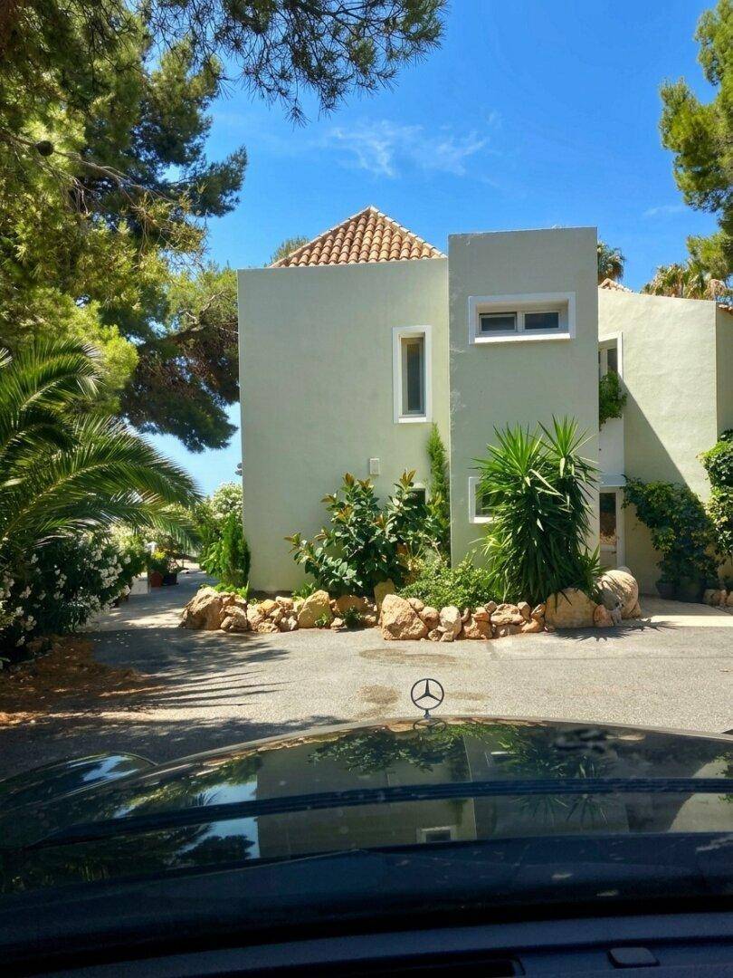 Villa mit heller Fassade, umgeben von mediterranen Bäumen und Sträuchern.