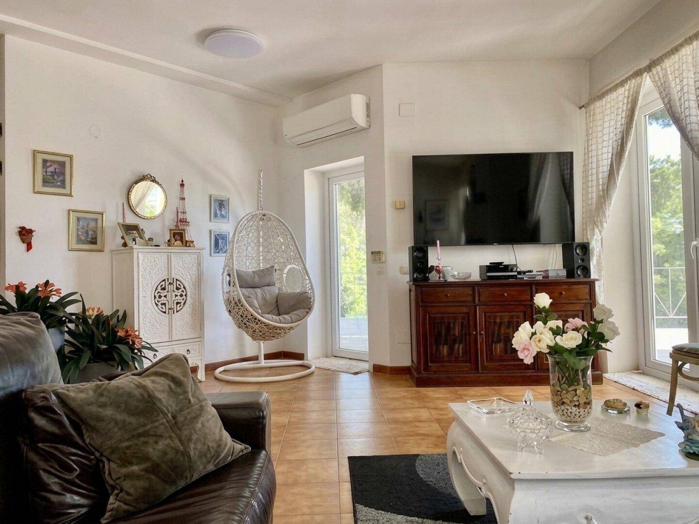 Helles Wohnzimmer mit Klimaanlage, Hängesessel und Zugang zur Terrasse.