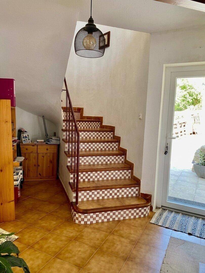 Flur mit Treppe, die mit gemusterten Fliesen verziert ist, und Zugang nach draußen.