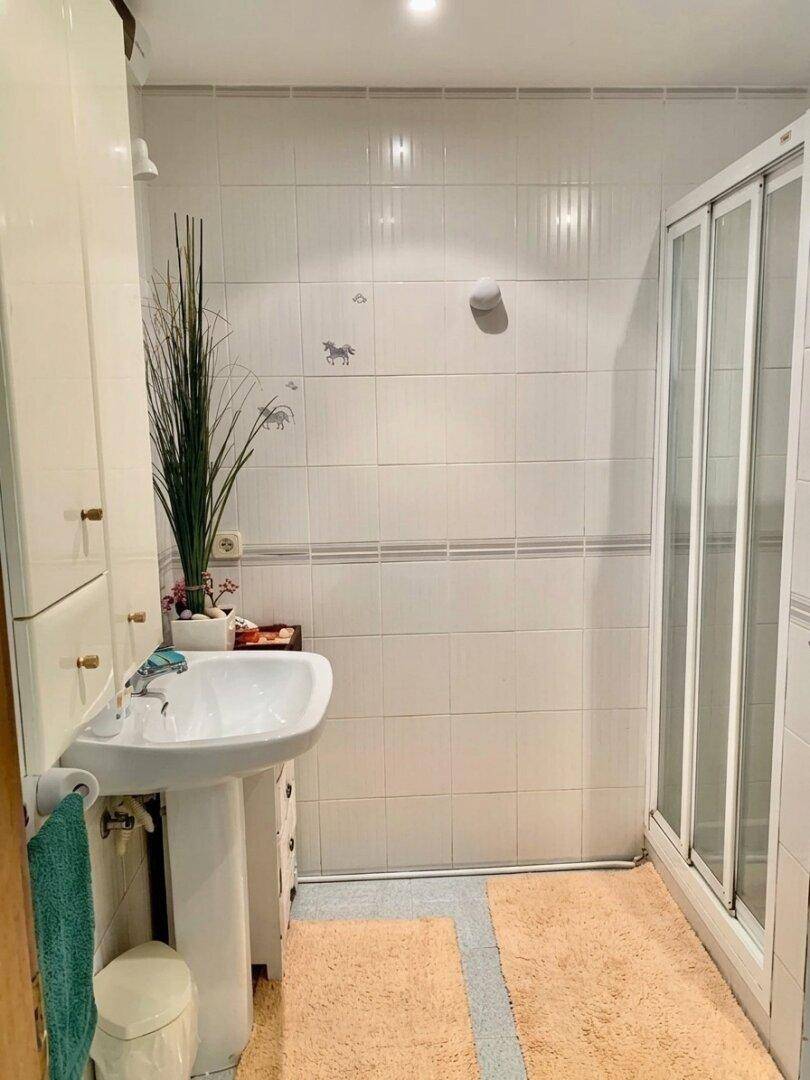 Helles Badezimmer mit Duschkabine, Standwaschbecken und weißen Fliesen.