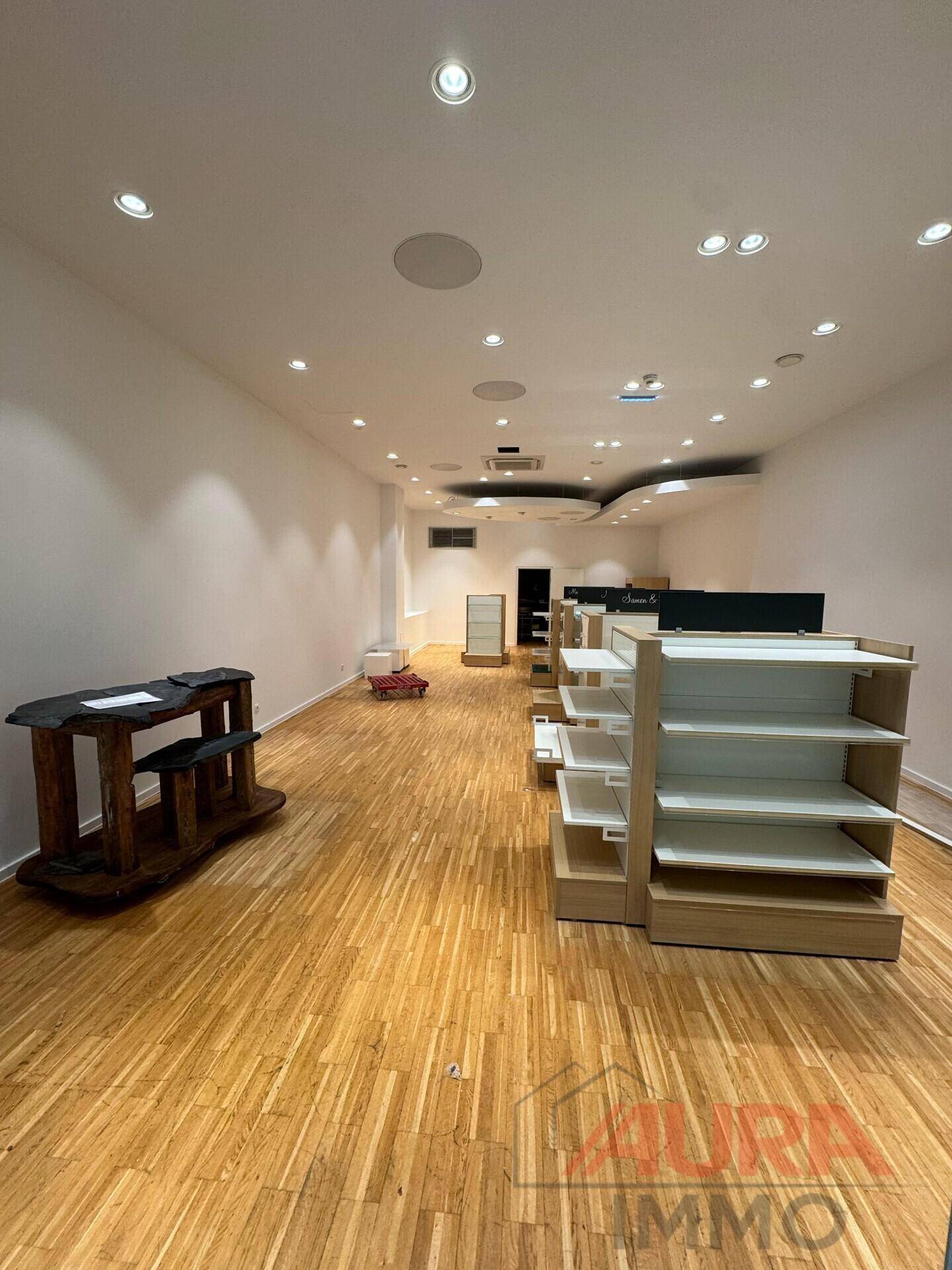 Langer, leerer Ladenraum mit Holzboden, weißen Wänden und moderner Deckenbeleuchtung.