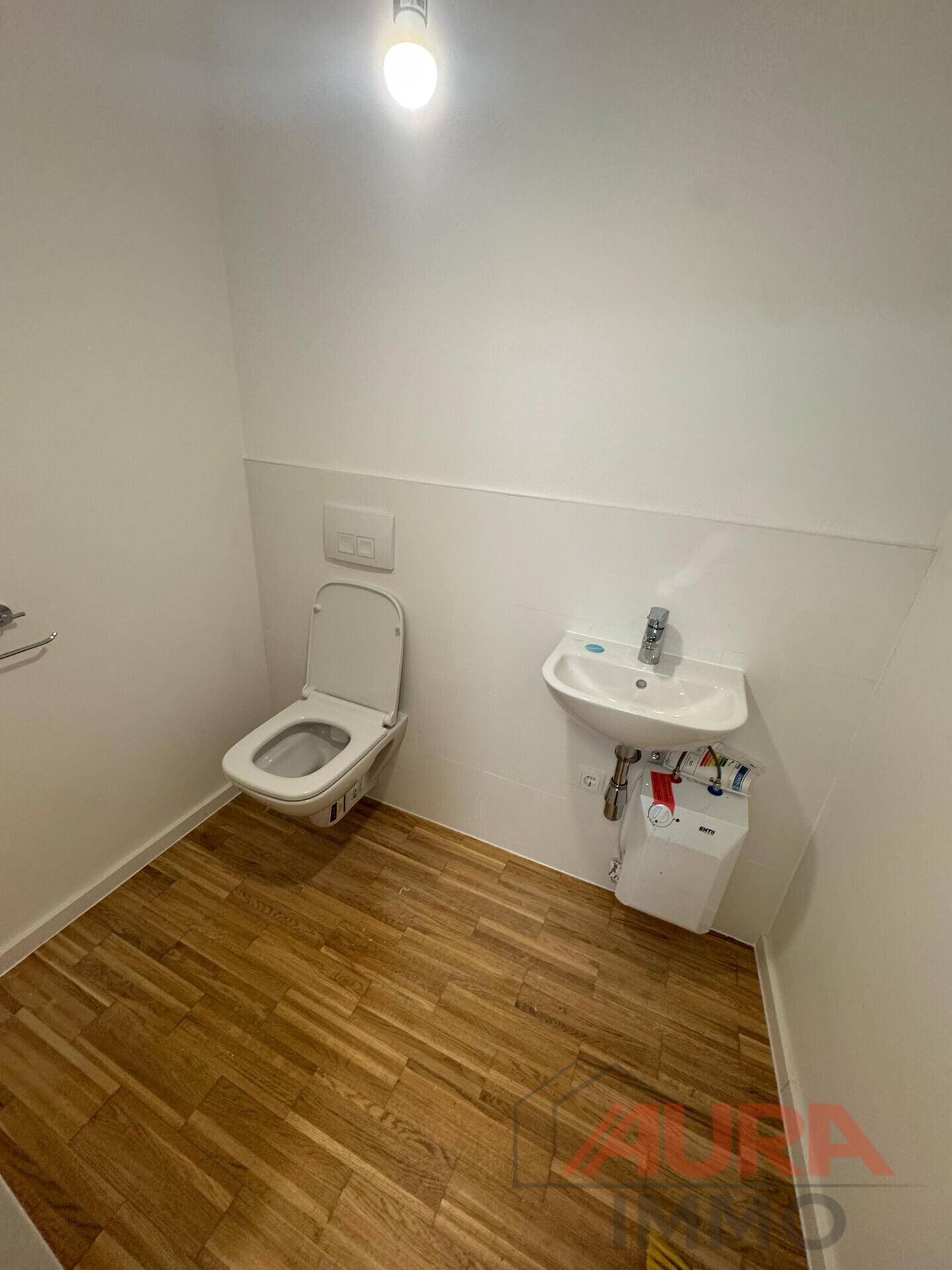 Kleine Toilette mit wandhängendem WC, Waschbecken und Holzboden.