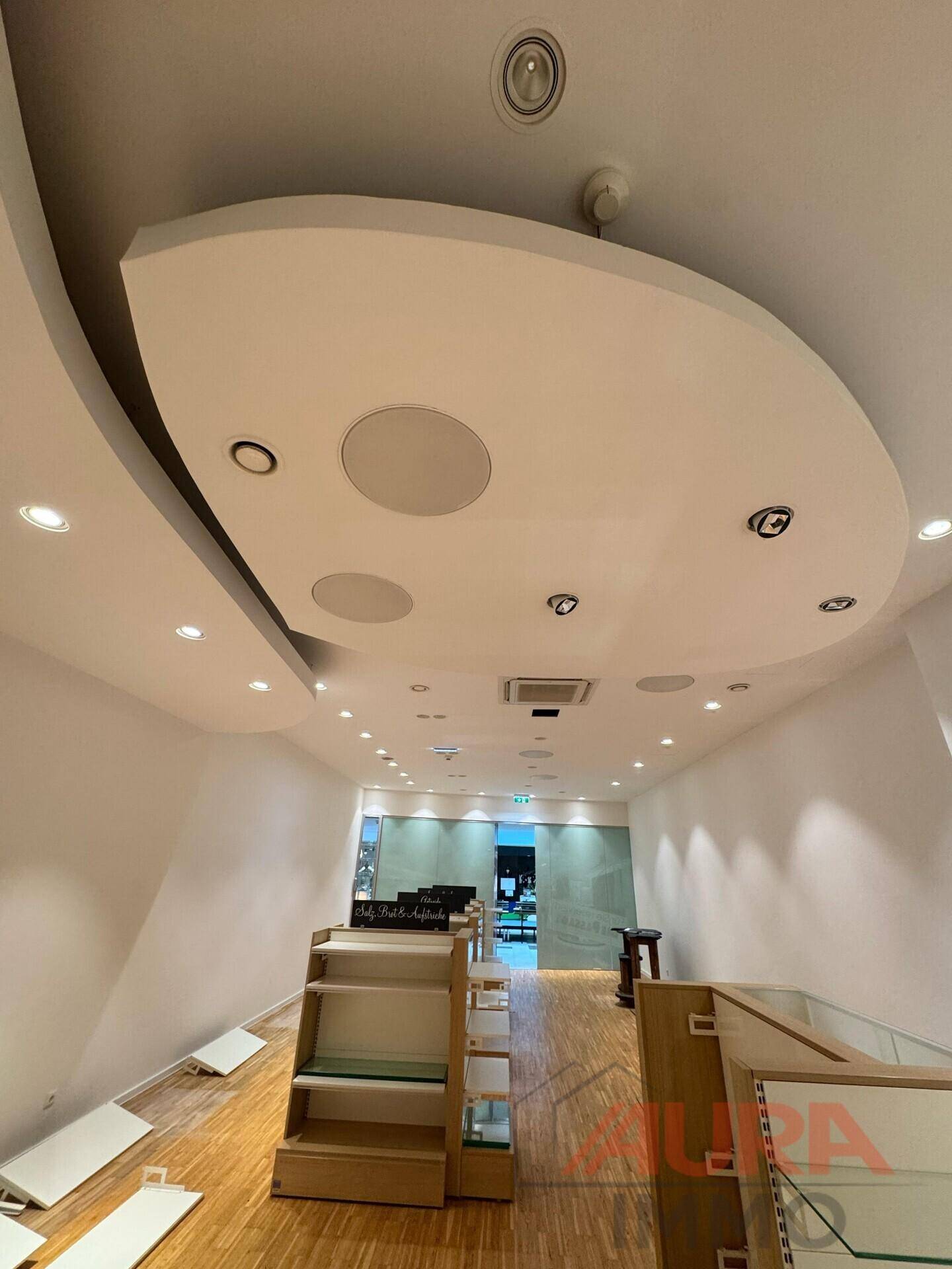 Blick zur Decke des Ladenraums mit geschwungenen Designelementen, Einbaustrahlern und Lautsprechern.