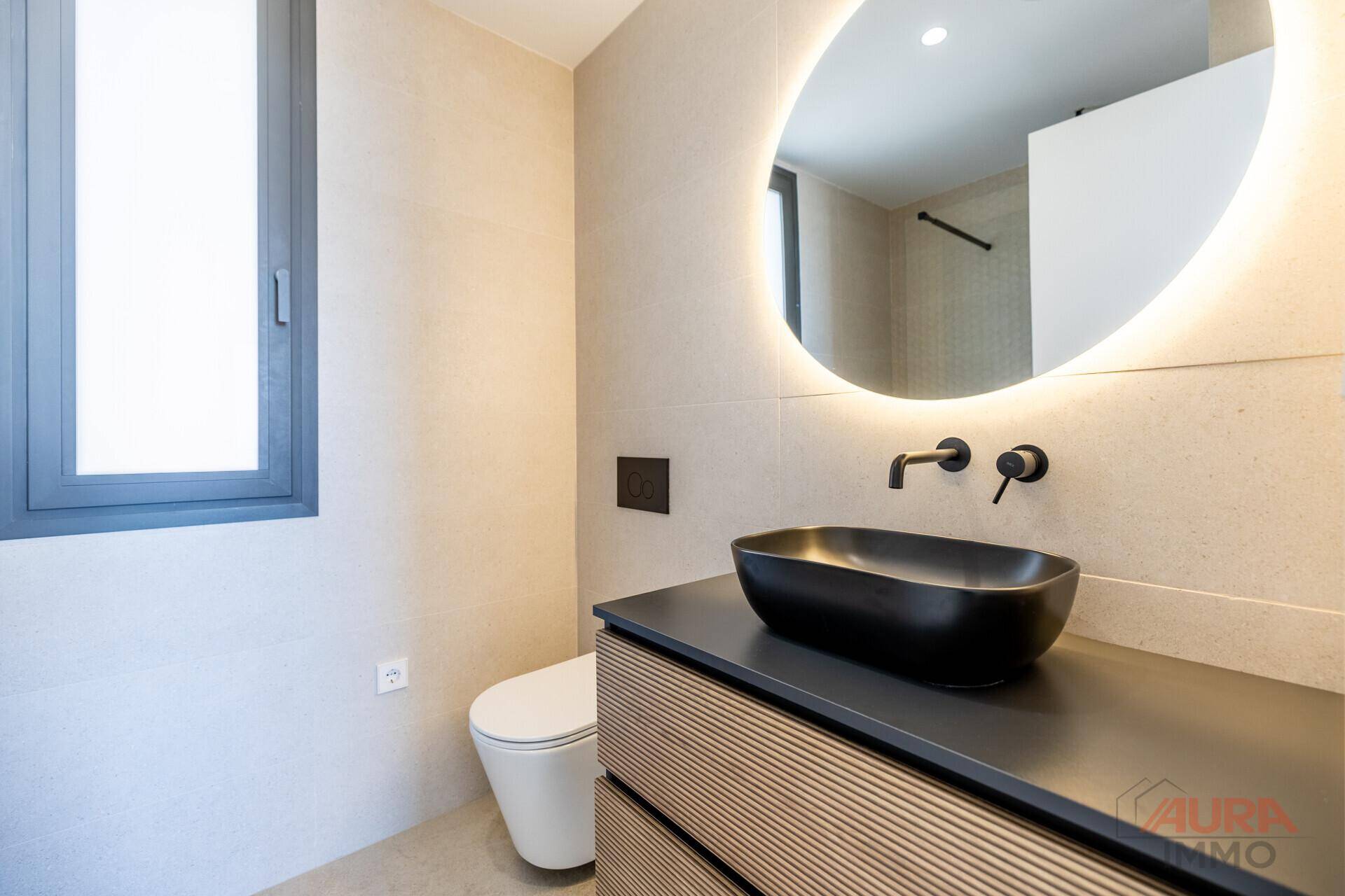 Modernes Badezimmer mit schwarzem Aufsatzwaschbecken, beleuchtetem Spiegel und WC.