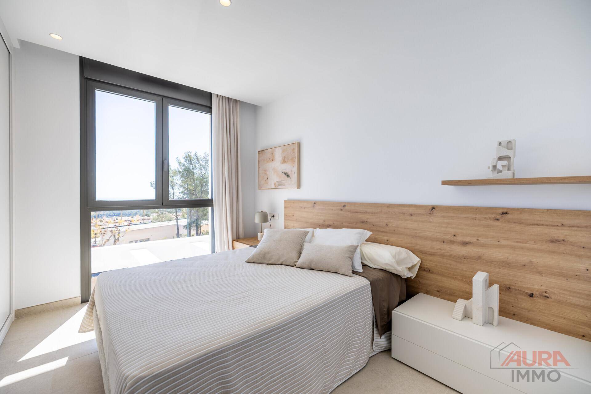 Helles Schlafzimmer mit Doppelbett, Holzkopfteil und großen Fenstern mit Ausblick.