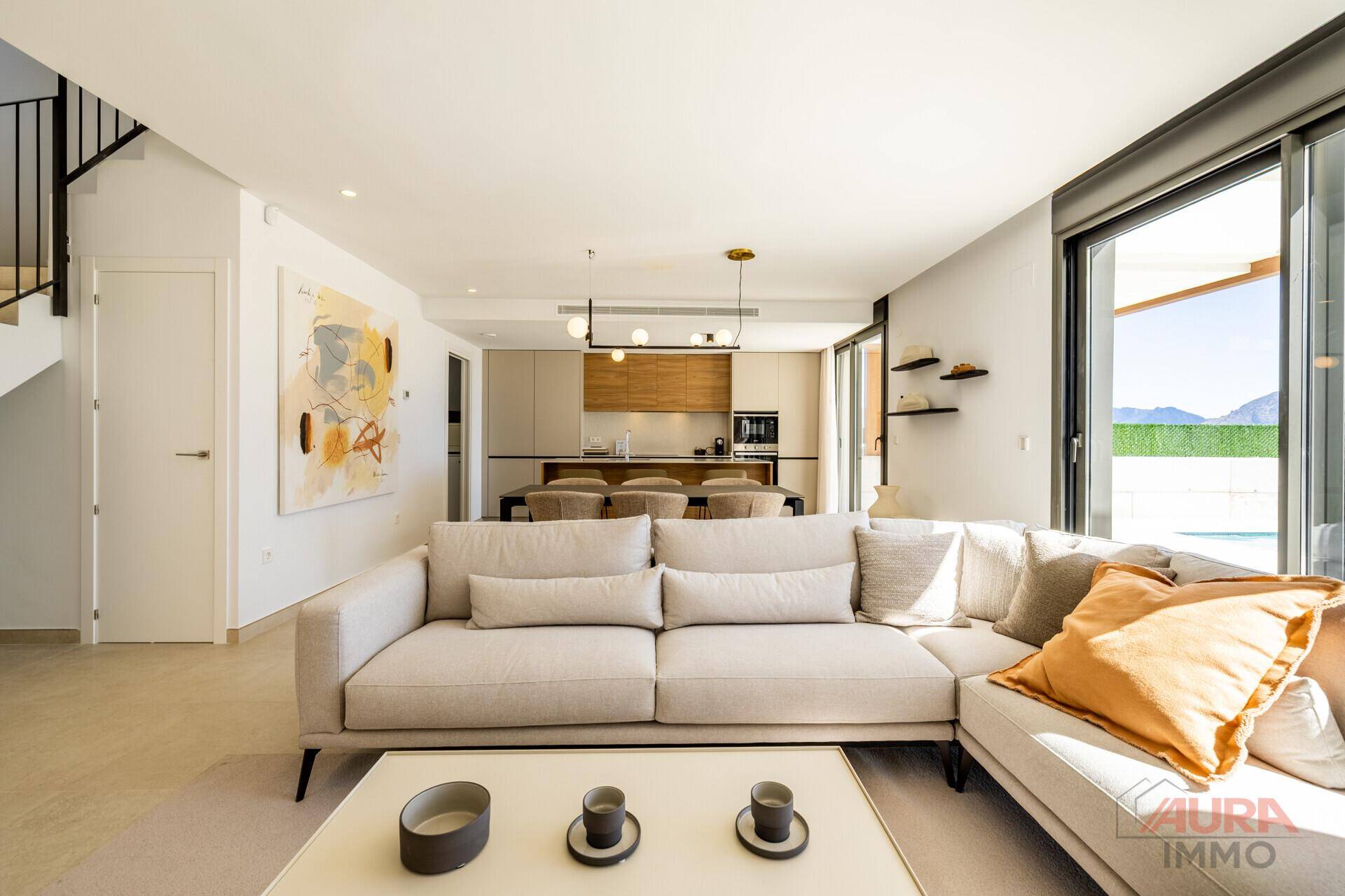 Offener Wohnbereich mit beigem Sofa, Essbereich, moderner Küche und Treppenaufgang.