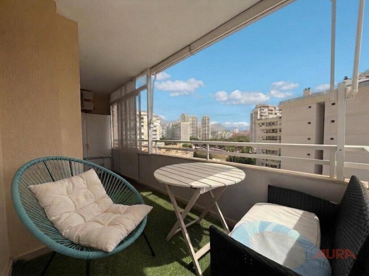 Verglaster Balkon mit Sitzgelegenheiten und weitem Blick auf die Stadt und umliegende Gebäude.