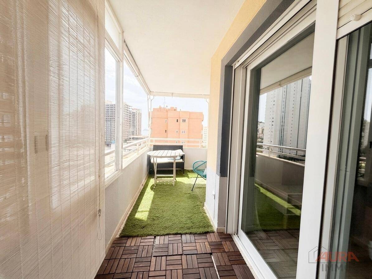 Heller, verglaster Balkon mit Kunstrasen und Holzbodenfliesen, zugänglich vom Innenbereich.