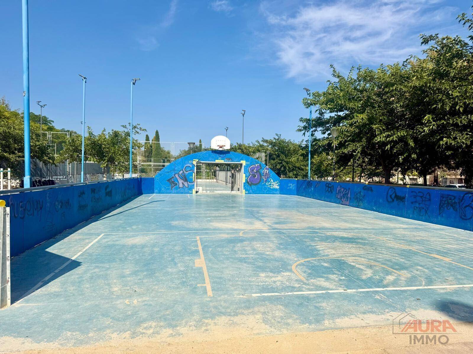 Blauer Basketballplatz im Freien mit Graffiti-Wänden und einem klaren, sonnigen Himmel.
