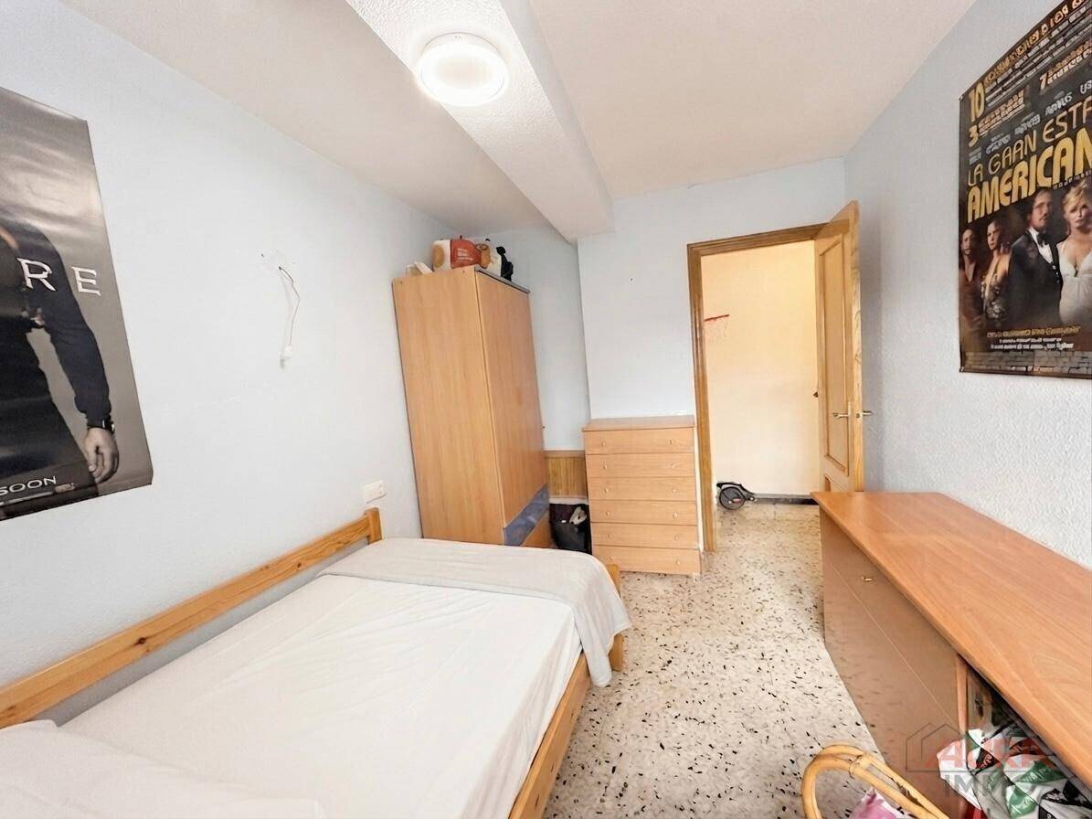 Schlafzimmer mit Einzelbett, Holzmöbeln und Terrazzoboden, dekoriert mit Postern.