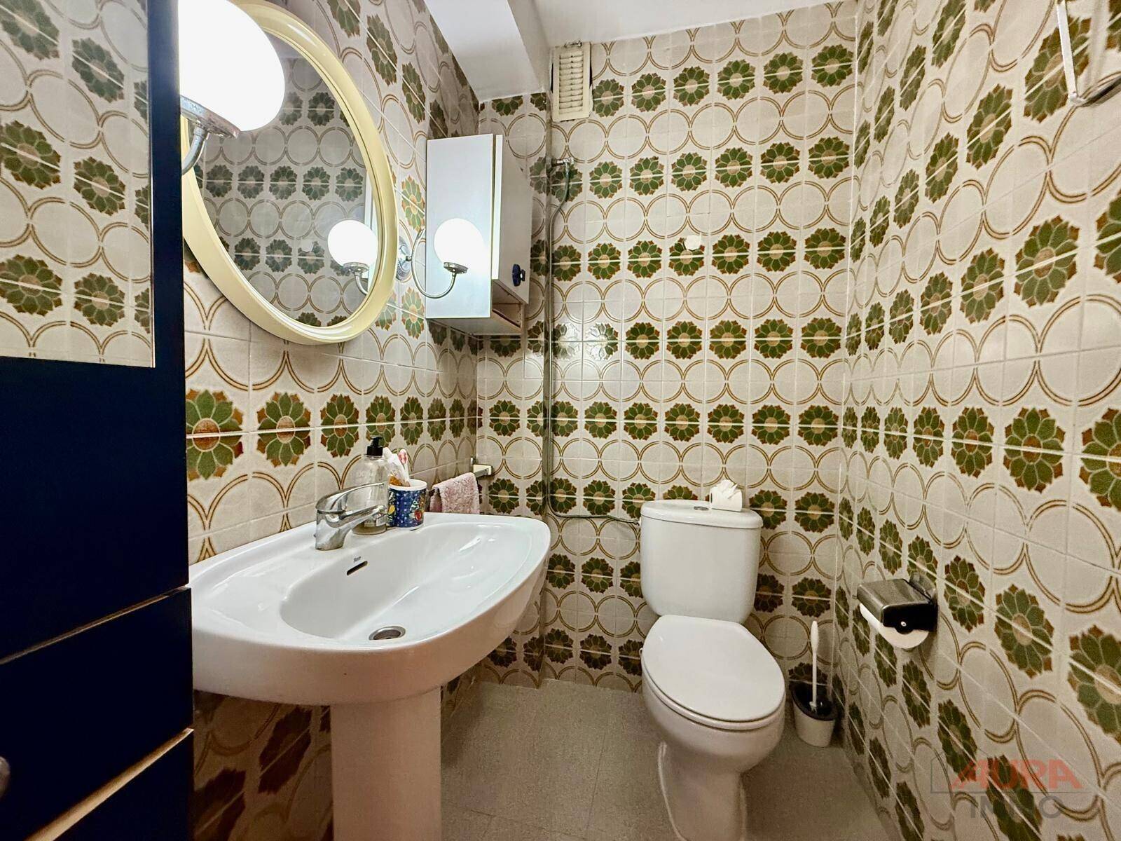Badezimmer mit gemusterten Fliesen, Waschtisch und Toilette im Stil der 80er Jahre.