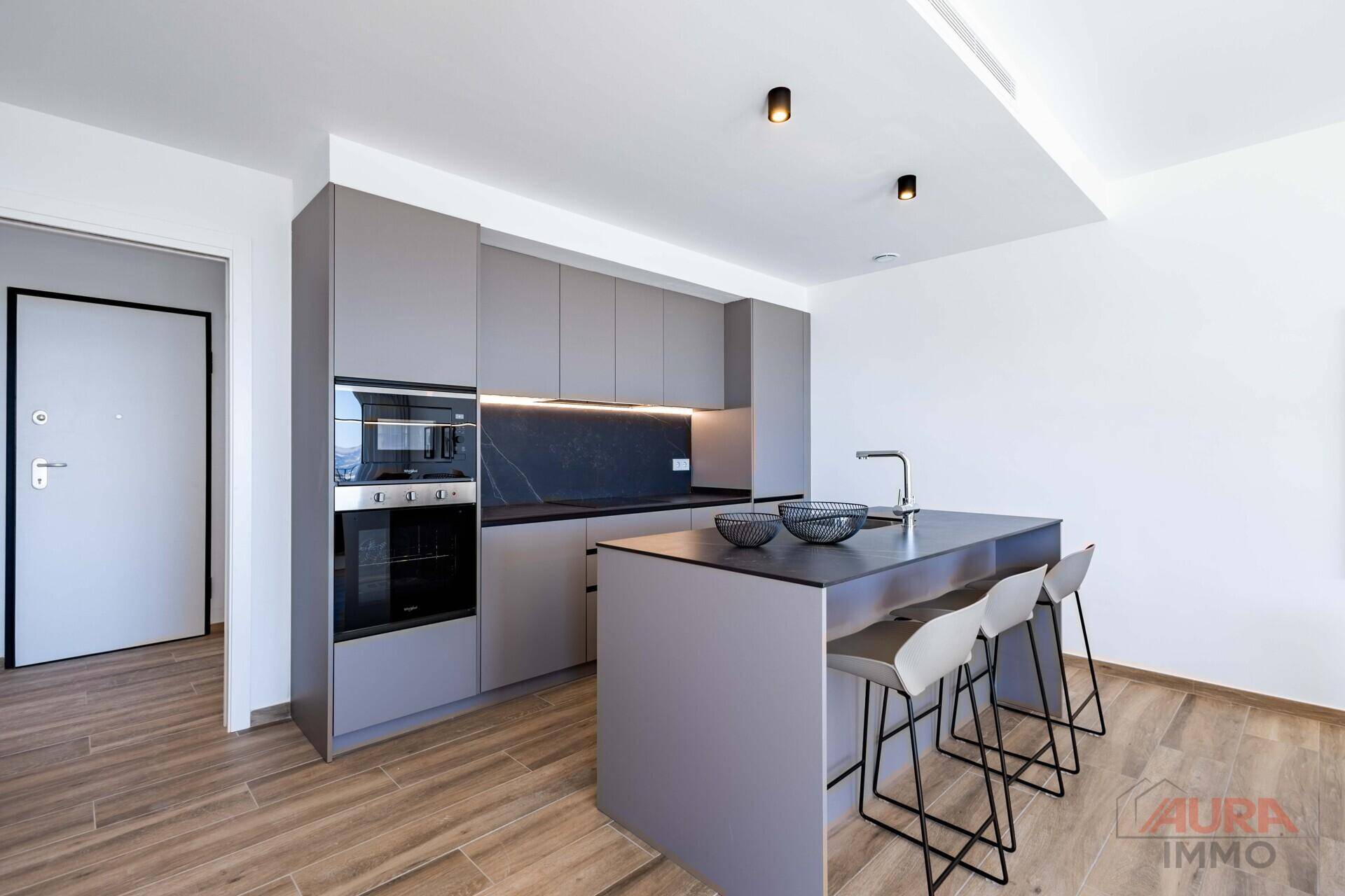 Moderne Küche mit grauen Schränken, Kücheninsel und integrierten Elektrogeräten.