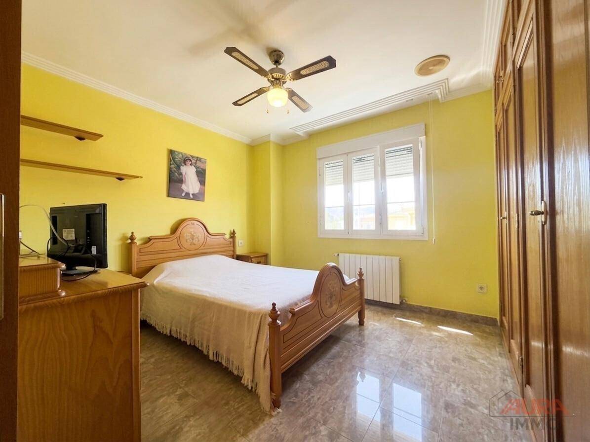 Farbenfrohes Schlafzimmer mit Doppelbett, gelben Wänden, Deckenventilator und Holzmöbeln.