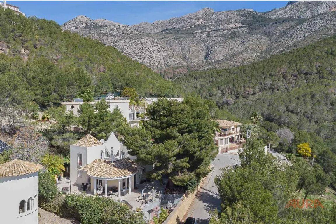 Panoramablick auf die Villa in einer grünen Hügellandschaft mit Bergen im Hintergrund.