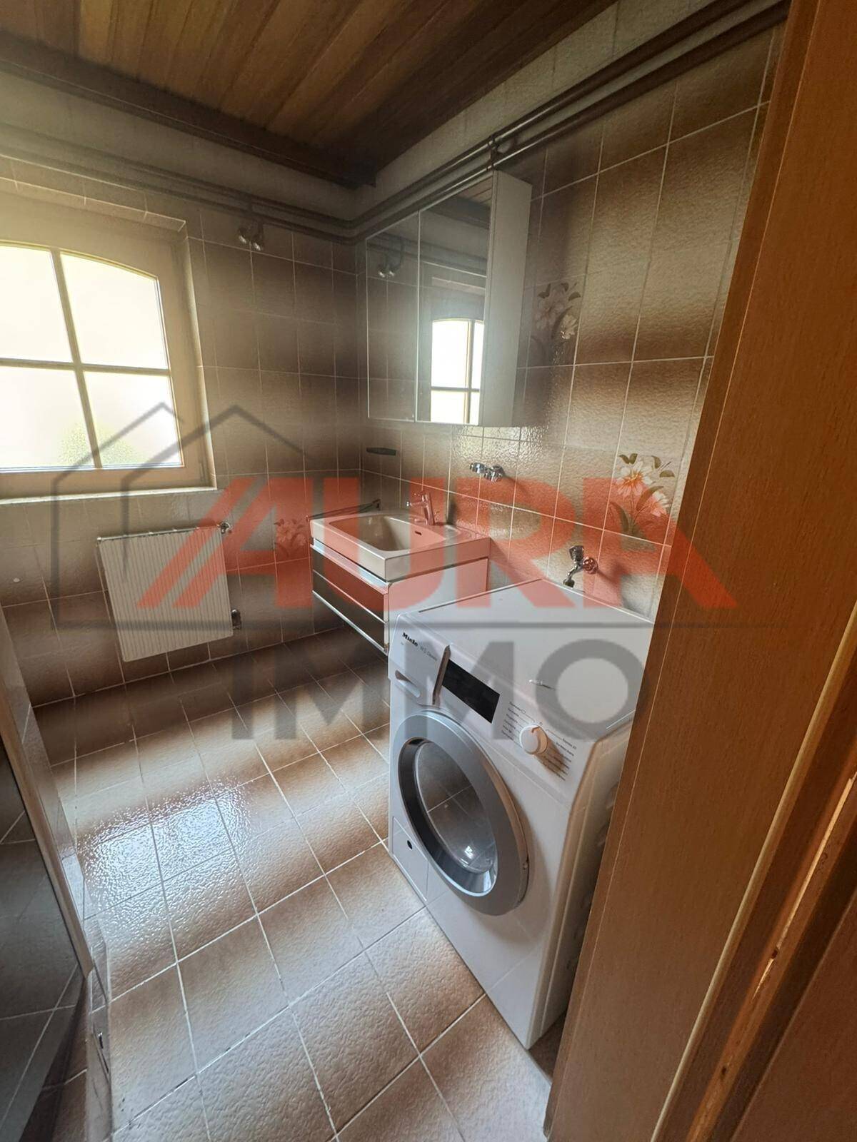 Funktionales Badezimmer mit Fliesenboden, Waschmaschine und Fenster für natürliche Belüftung.