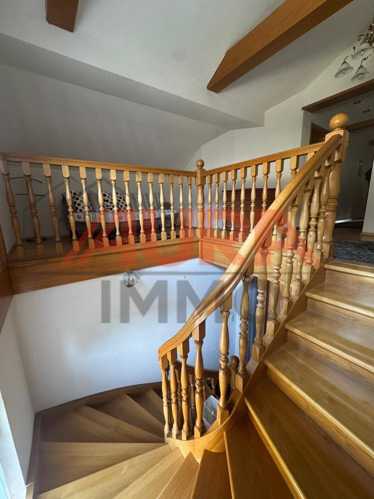 Elegante Holztreppe mit gedrechseltem Geländer und sichtbaren Holzbalken, die nach oben führt.