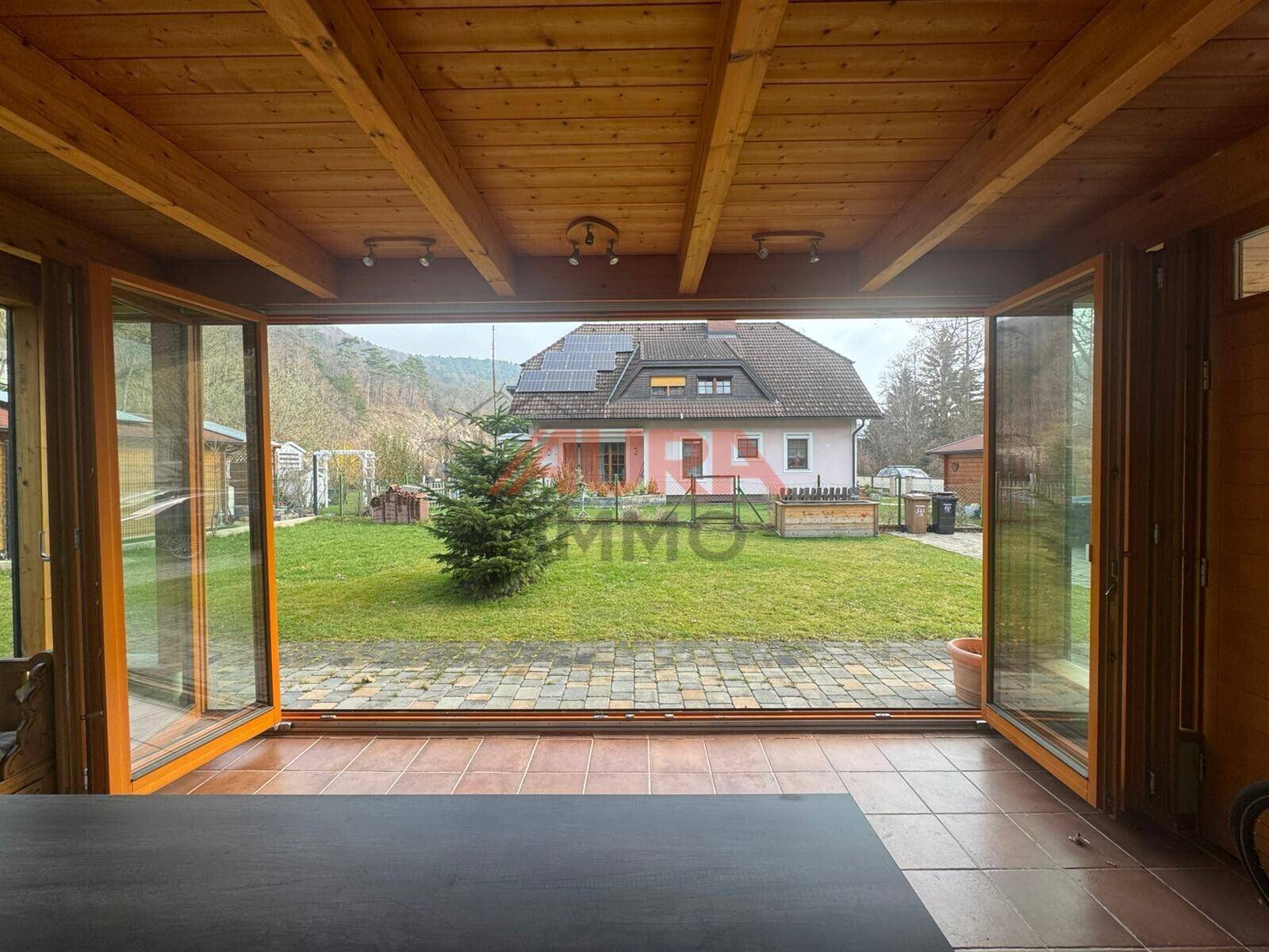 Offener Wintergarten mit Blick auf den Garten und das gegenüberliegende Haus mit Solaranlage.