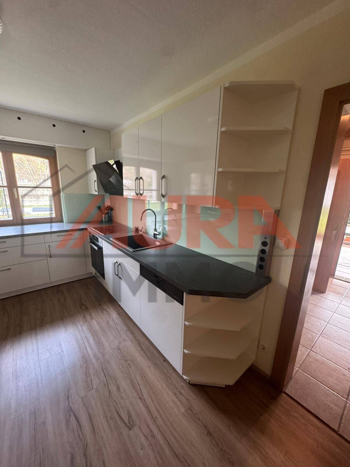 Moderne Einbauküche mit weißen Schränken, dunkler Arbeitsplatte und offenem Regal.