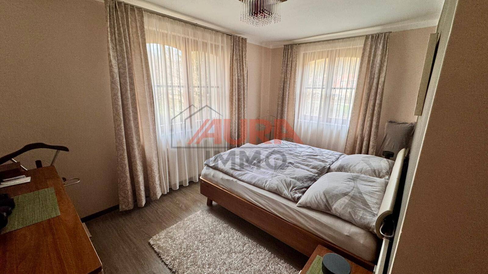 Gemütliches Schlafzimmer mit Doppelbett, Laminatboden und zwei Fenstern für natürliches Licht.