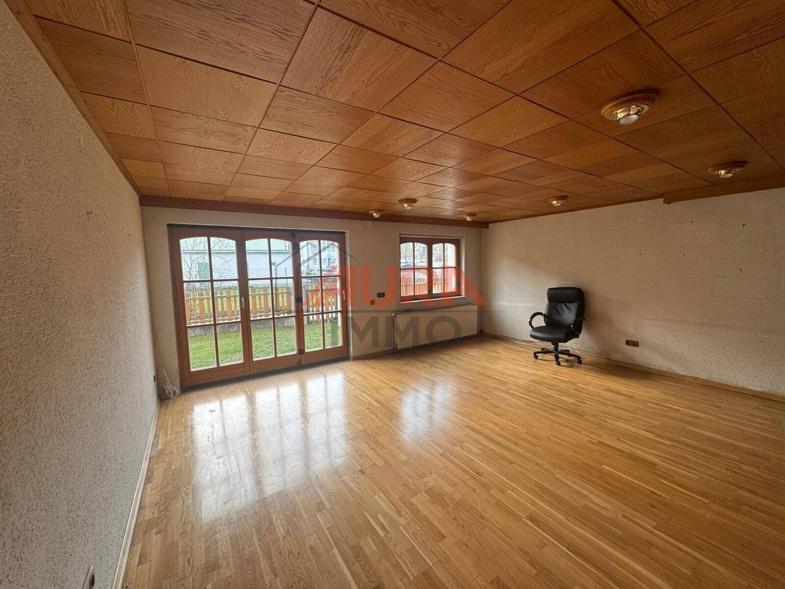 Geräumiges Wohnzimmer mit Holzboden, Holzdecke und Zugang zum Garten, ideal für Familien.