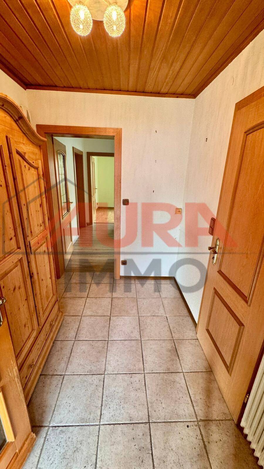 Flur mit Fliesenboden, Holzdecke und traditionellem Holzschrank.