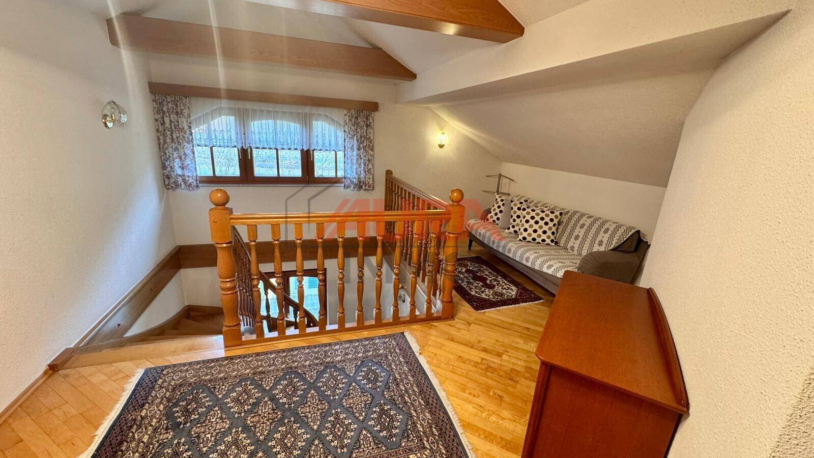 Gemütlicher Treppenabsatz im Dachgeschoss mit Holzboden, Sofa und Fenster, unter sichtbaren Holzbalken.