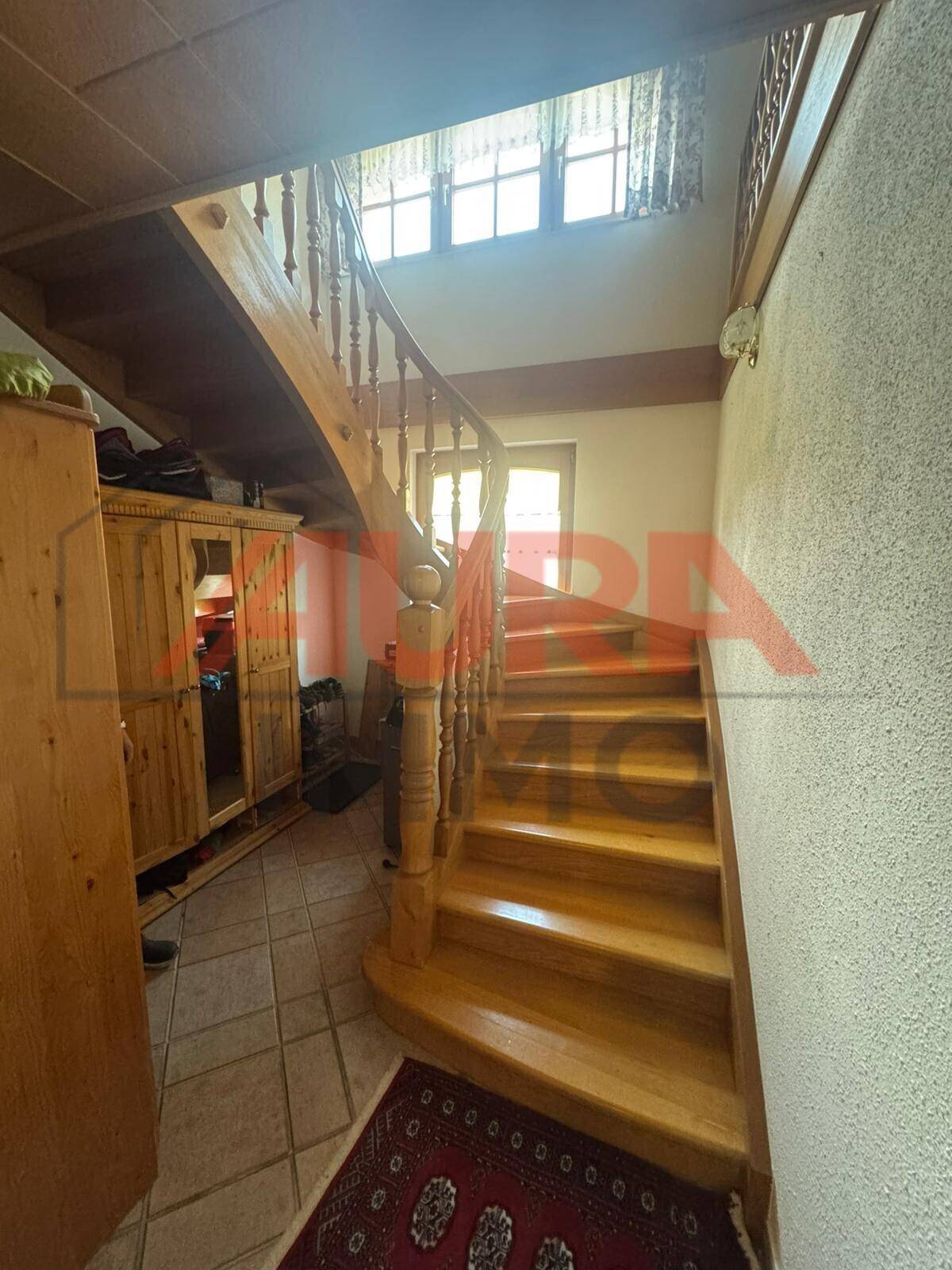 Traditionelle Holztreppe mit Geländer, die in den oberen Bereich führt, mit Fliesenboden unten und Fenster.