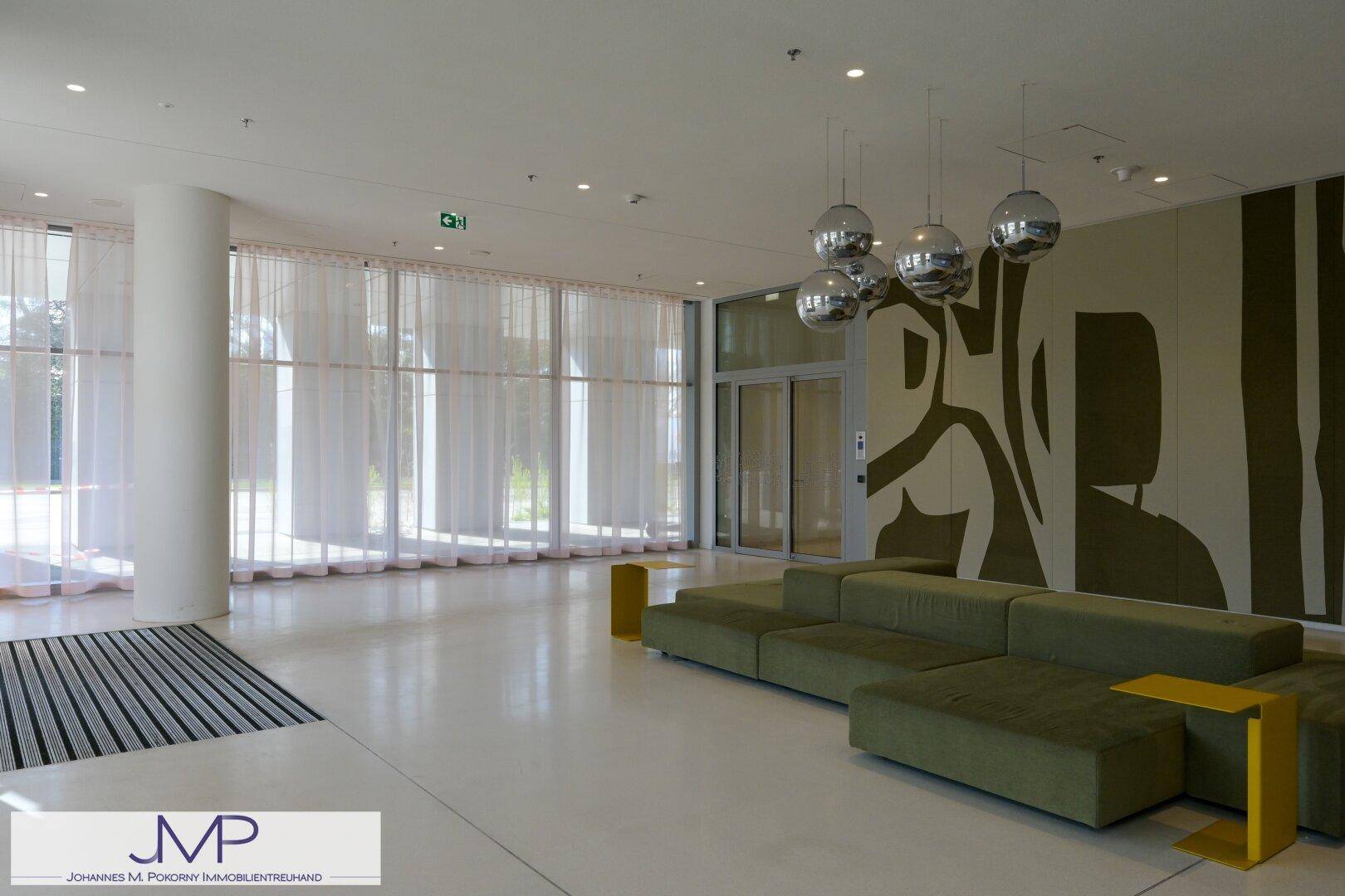Helle Lobby mit großen Fenstern, modernen Sitzmöbeln und dekorativen Kugellampen.